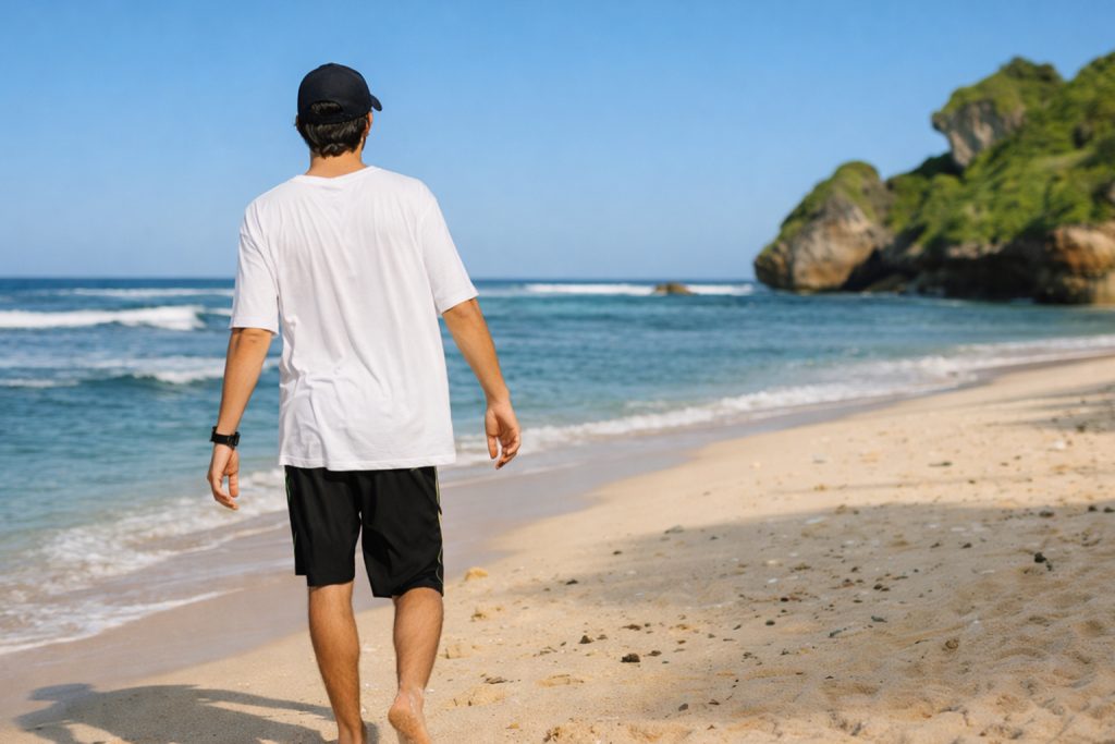 Hombre caminando por la playa tras un injerto capilar en verano evitando exposición solar directa