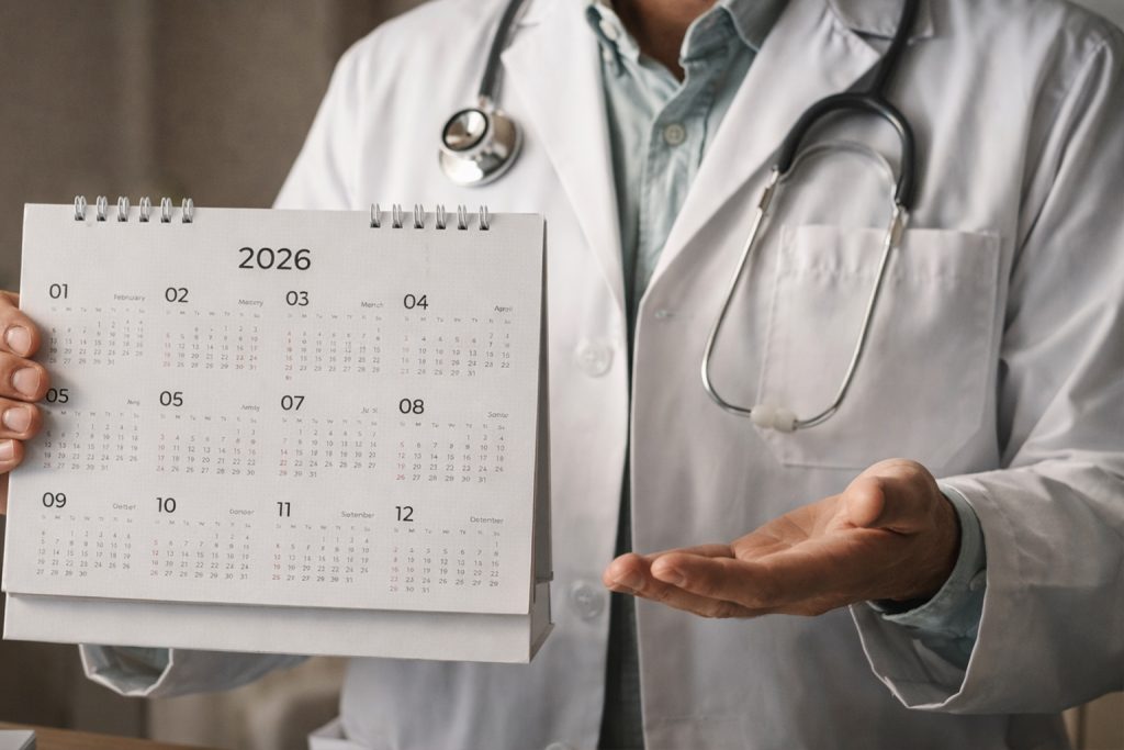 Médico con bata blanca sosteniendo un calendario anual y explicando los tiempos del proceso de injerto capilar